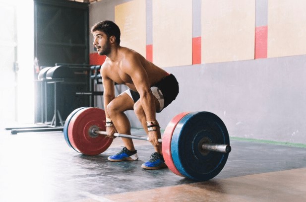 Homem levantando pesos em uma academia, demonstrando a técnica correta para equilibrar peso e repetições durante o treino de força. 