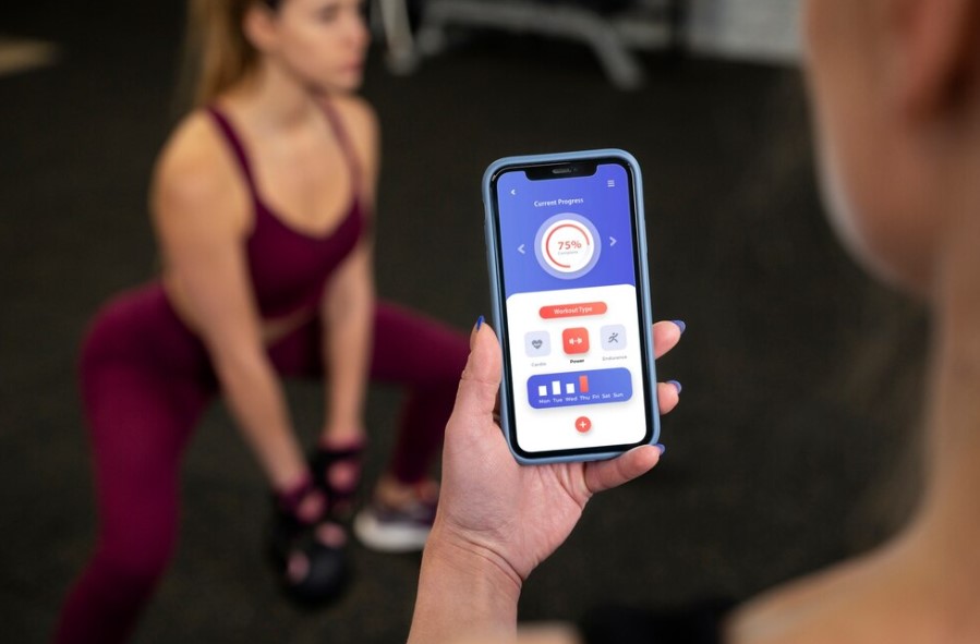 Celular mostrando aplicativo de gamificação de treino, com mulher exercitando-se ao fundo.