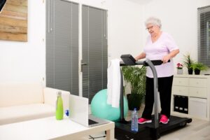 Senhora em sua sala, utilizando um esteira para idosos em sua rotina de exercícios.