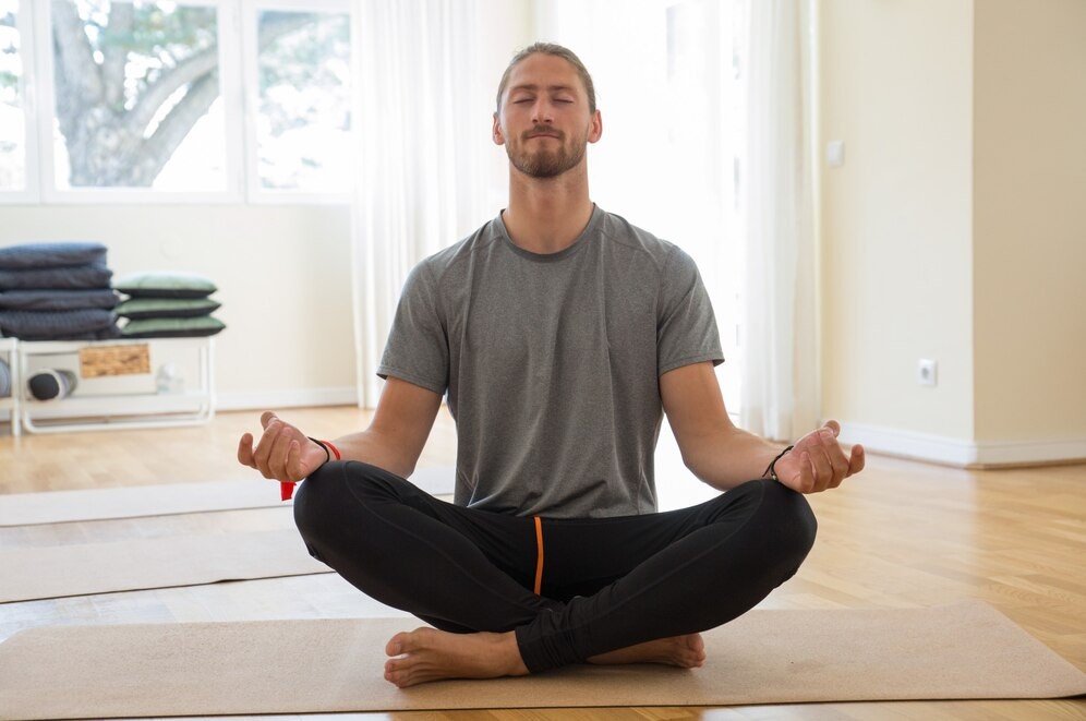 Homem sentado em posição de meditação em um ambiente tranquilo, refletindo sobre o impacto positivo do exercício físico no bem-estar mental, promovendo relaxamento e foco.