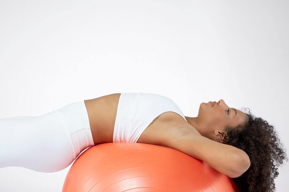 Mulher se alongando com uma bola de yoga para melhorar as dores nas costas