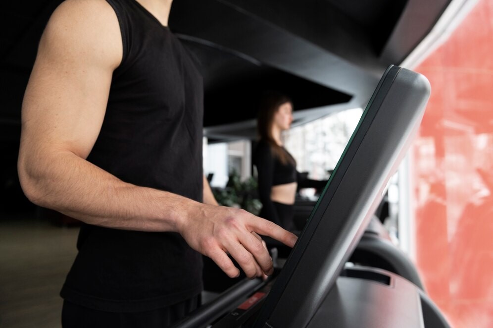 Homem programando seu treino no painel da esteira na academia.