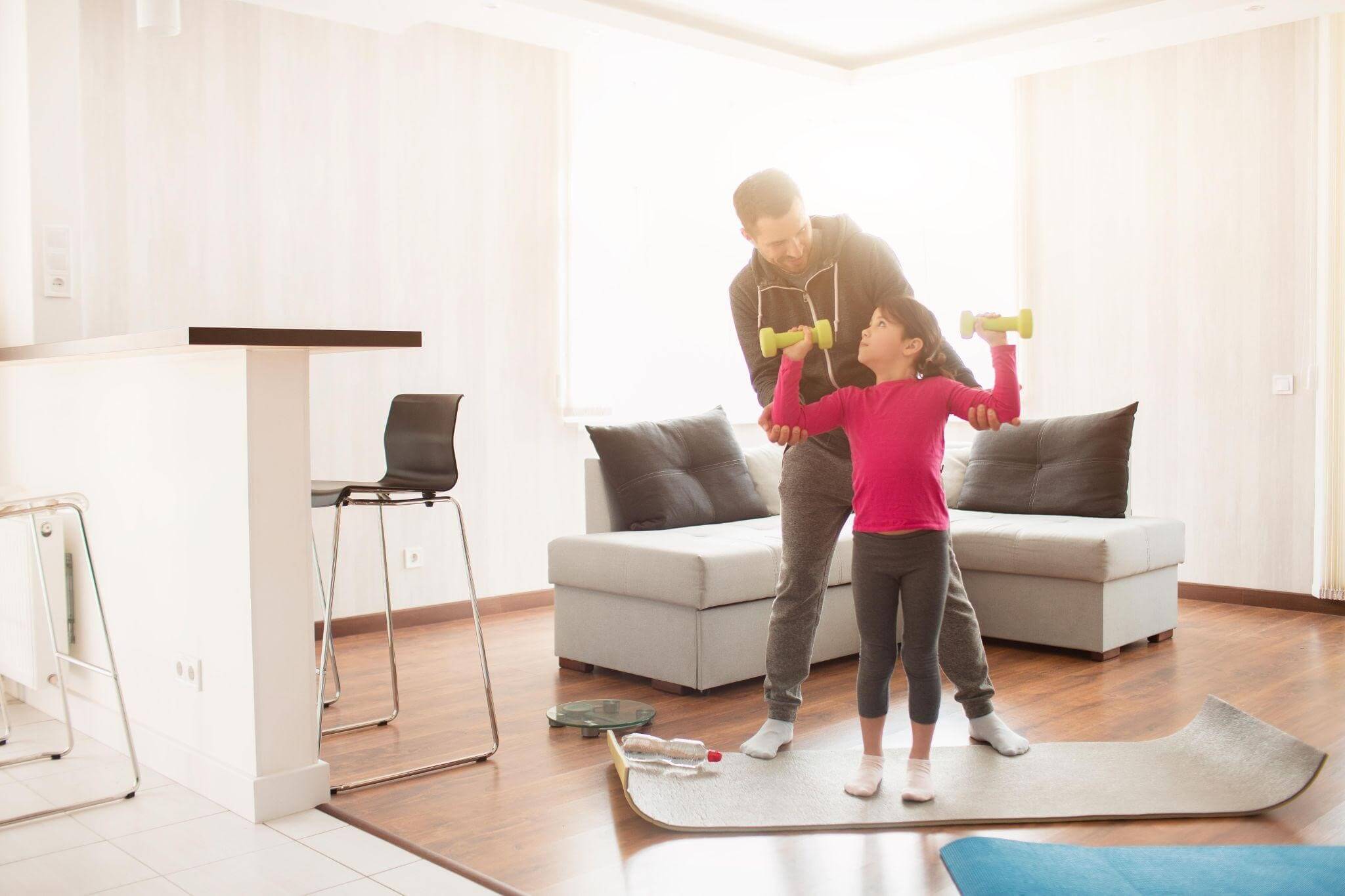 Pai realizando treino leve e divertido com sua filha na sala de casa.