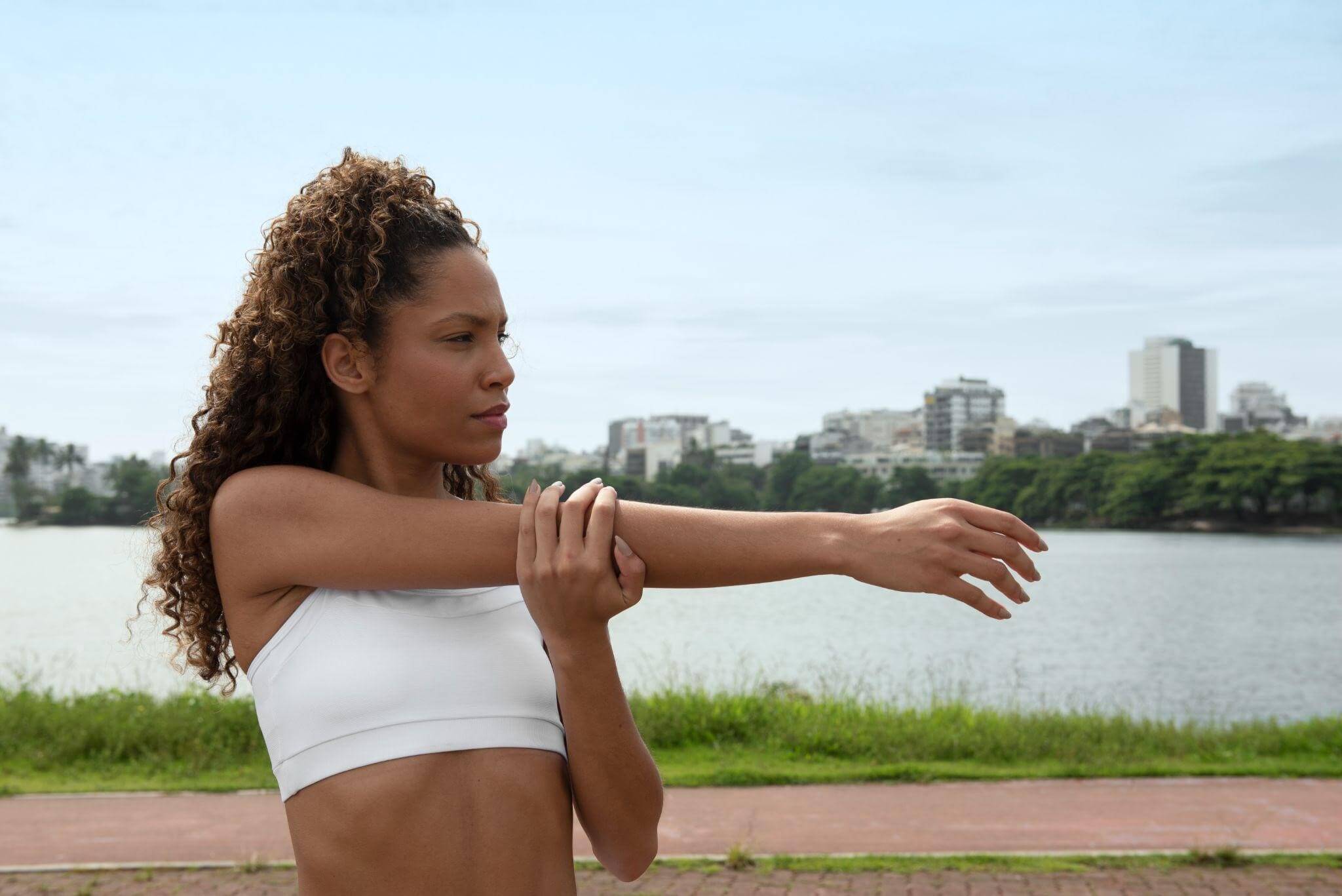 Mulher se alongando em um parque a céu aberto.