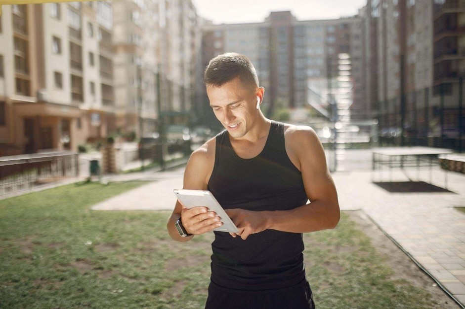 Homem no jardim do condomínio buscando por aparelhos de academia Athletic através do seu tablet.