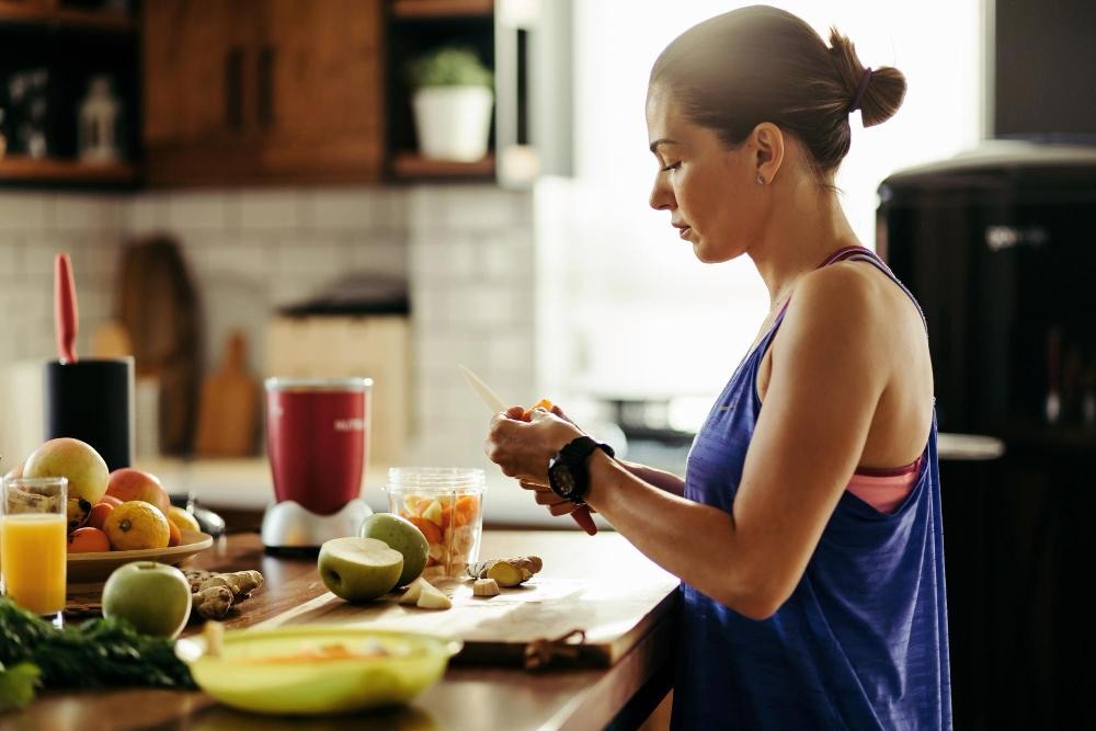 Mulher adulta com roupas de academia preparando uma salada de frutas